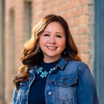 Smiling woman in denim jacket outside building.