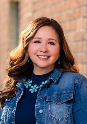 Smiling woman in denim jacket outside building.